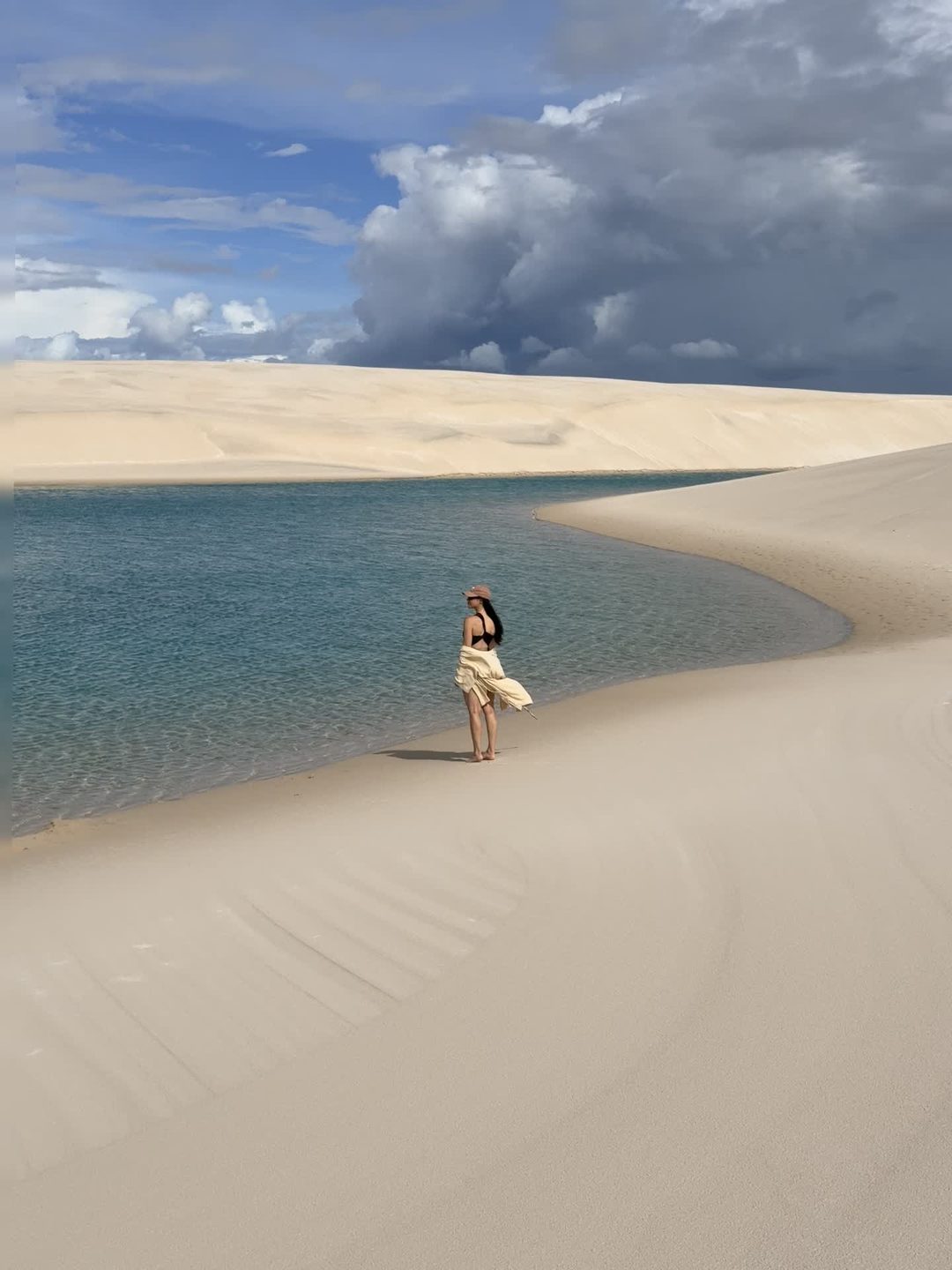 Miriã caminhando entre as dunas e uma lagoa nos Lençóis Maranhenses